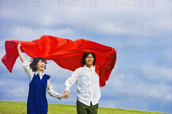 Asian couple holding blanket in wind