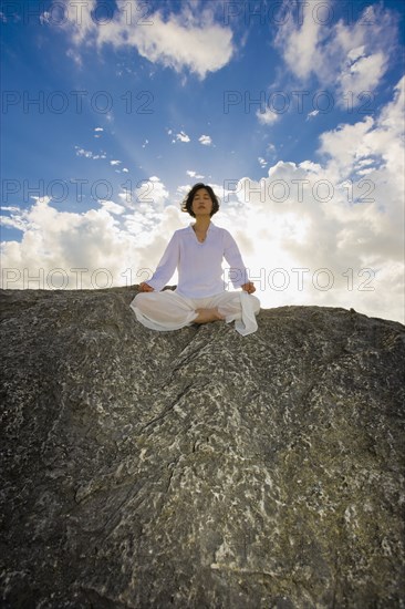 Asian woman meditating on rock