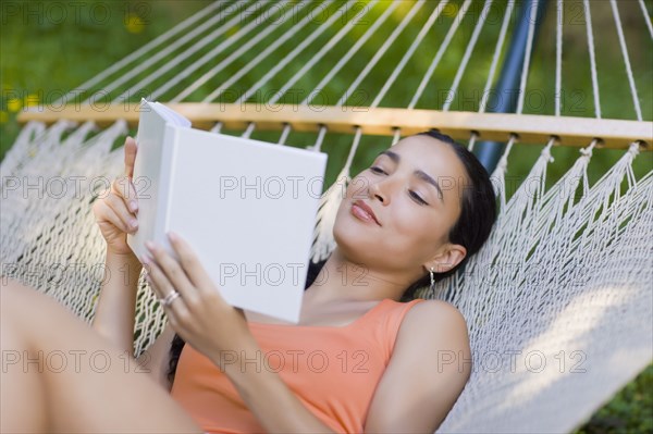 Hispanic woman laying in hammock reading