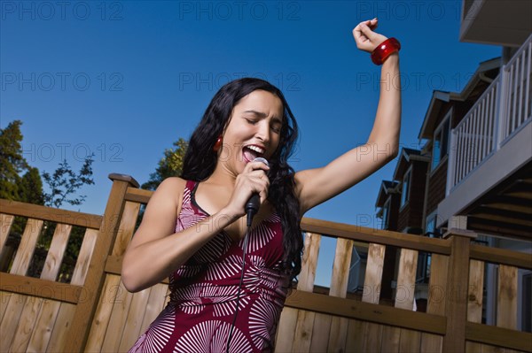 Hispanic woman singing karaoke in backyard