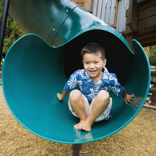 Mixed race boy sliding in playground
