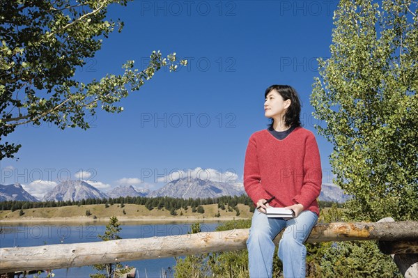 Japanese woman sitting on fence with mountains in background
