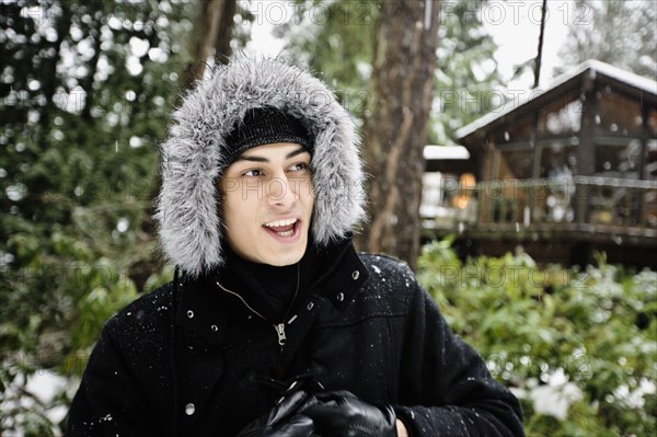 Mixed race man in hooded coat outdoors in snowfall