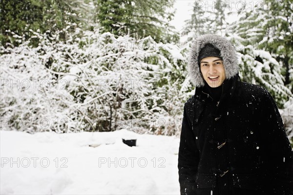 Mixed race man in hooded coat outdoors in snowfall