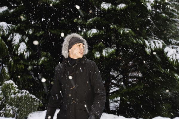 Mixed race man in hooded coat outdoors in snowfall