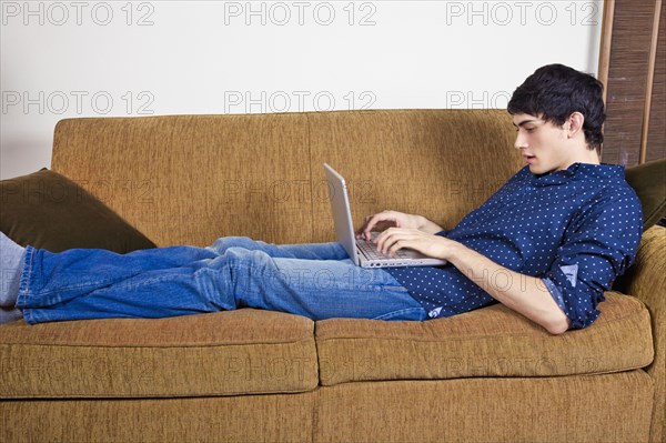 Mixed race man typing on laptop on sofa