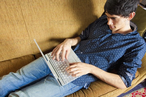 Mixed race man typing on laptop on sofa