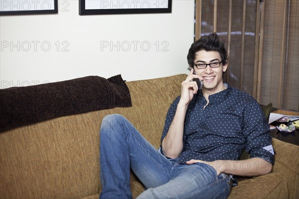 Mixed race man reclining on sofa talking on cell phone