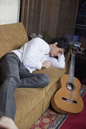 Mixed race man sleeping on sofa next to guitar