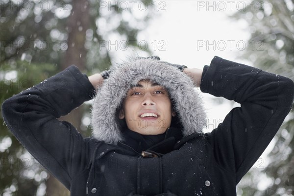 Mixed race man in hooded coat outdoors in snowfall