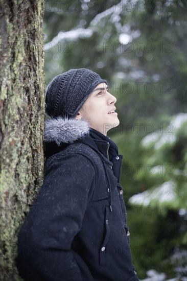 Mixed race man leaning against tree trunk