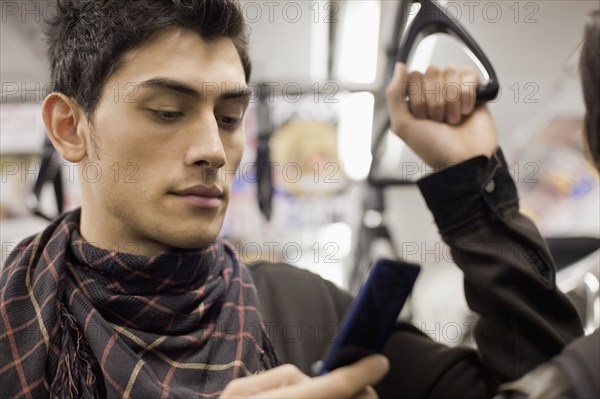 Close up of mixed race man text messaging with cell phone on subway