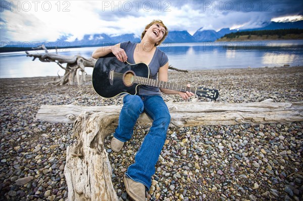 Caucasian woman playing guitar near lake