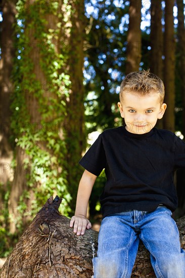 Caucasian boy sitting on log in forest