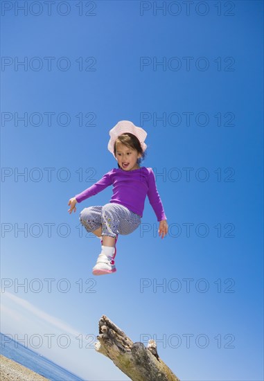 Low angle view of mixed race girl jumping from log on beach