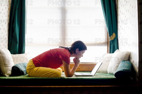 Japanese woman leaning on day bed reading laptop