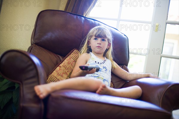 Caucasian girl sitting in armchair holding remote control