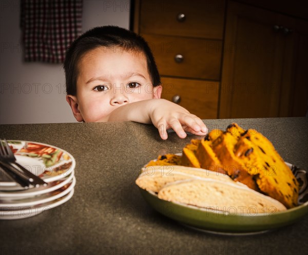 Mixed Race boy reaching for cake on counter