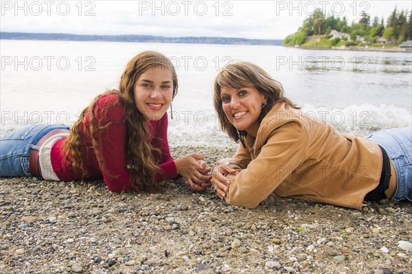 Smiling mother and daughter laying on rocky beach