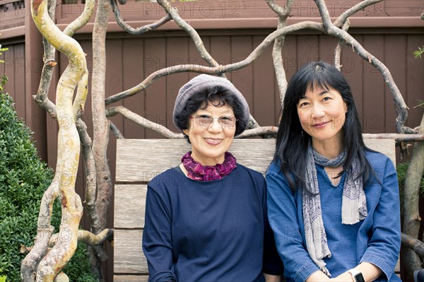 Older Japanese mother and daughter sitting on wooden bench