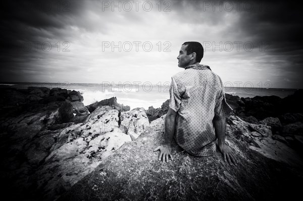 Pensive Caucasian man sitting on rocks at ocean