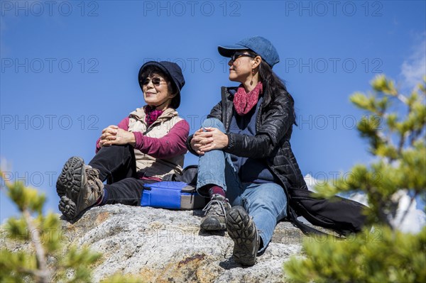 Older Japanese mother and daughter sitting on rock