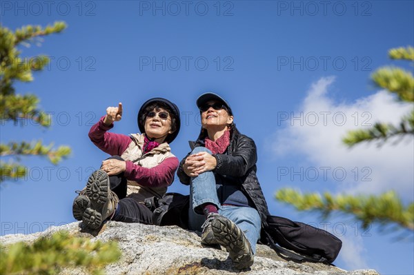 Older Japanese mother and daughter sitting on rock