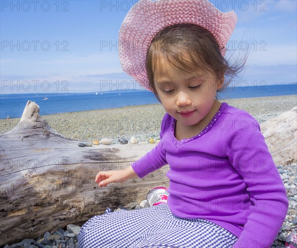 Mixed Race girl sitting on beach near log