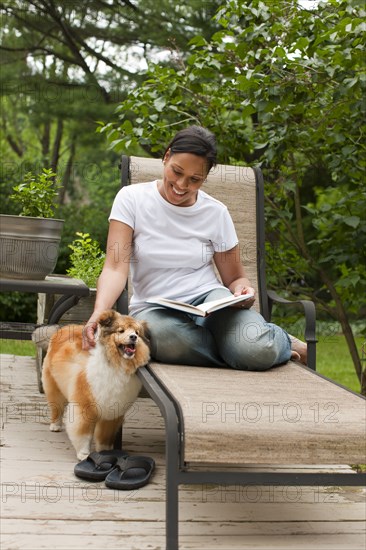 African American woman reading book and petting dog