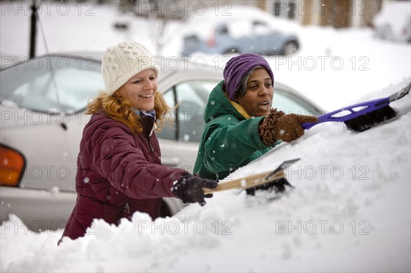 Two women scraping snow from windshield