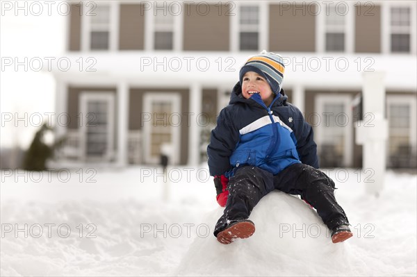 Mixed race boy sitting on large snowball