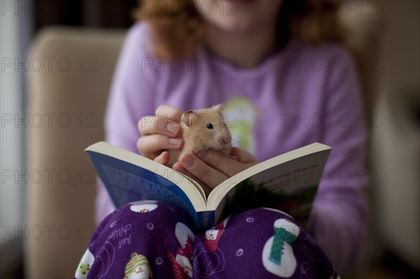 Caucasian girl sitting with book and pet hamster