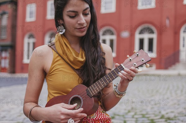 Mixed race woman playing ukulele on city street