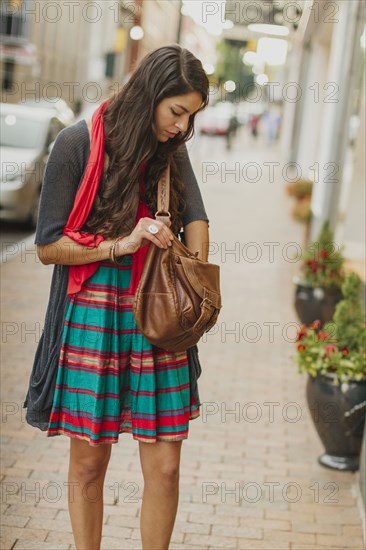 Mixed race woman digging in purse on city street