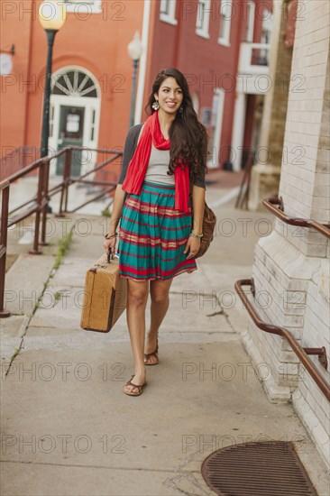 Mixed race woman carrying suitcase on city street