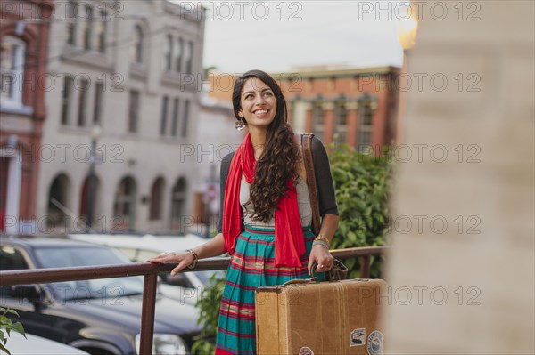 Mixed race woman carrying suitcase on city street