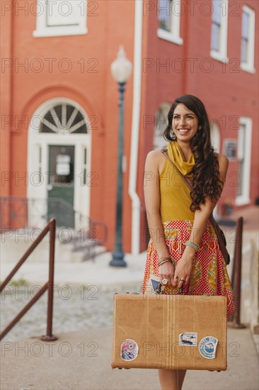 Mixed race woman carrying suitcase on city street