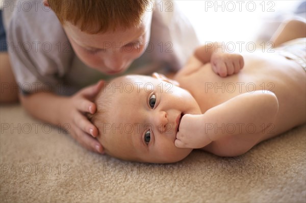 Caucasian boy kissing baby brother on carpet