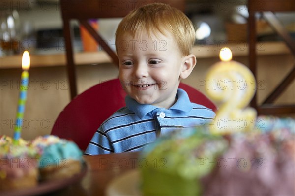Caucasian boy admiring birthday cake and cupcake