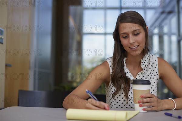 Mixed race businesswoman writing on notepad at desk
