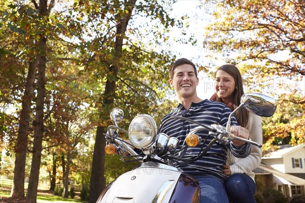 Couple riding scooter in suburban neighborhood