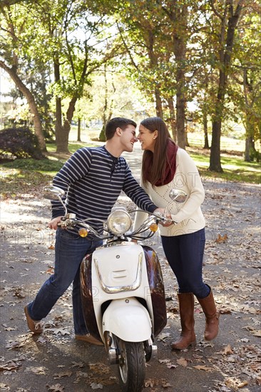 Couple kissing over scooter in suburban neighborhood