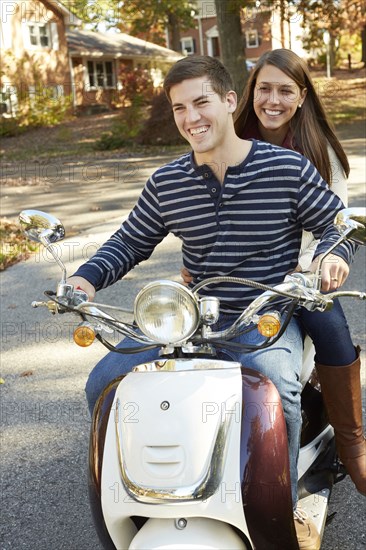 Couple riding scooter in suburban neighborhood