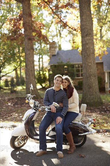 Couple sitting on scooter in suburban neighborhood