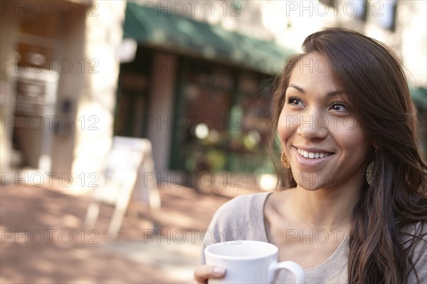 Mixed race woman drinking coffee on sidewalk