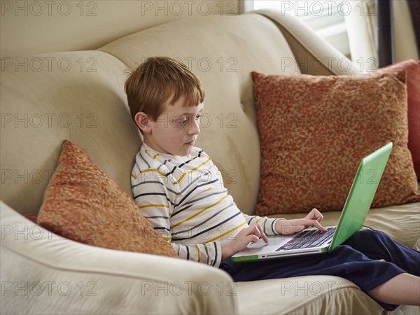 Caucasian boy using laptop on sofa