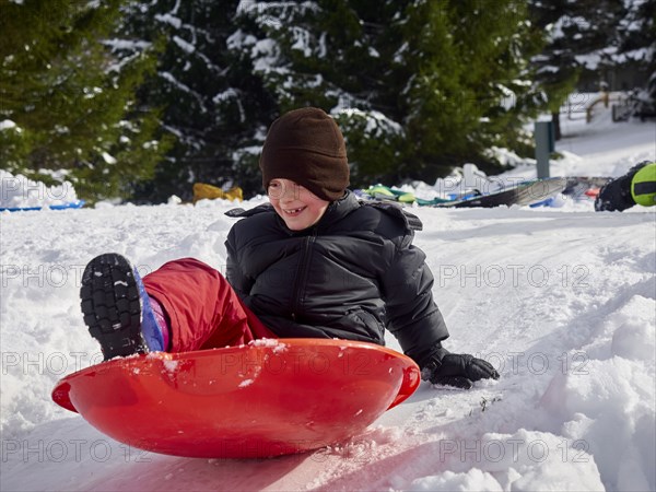 Caucasian boy sledding on snowy hill