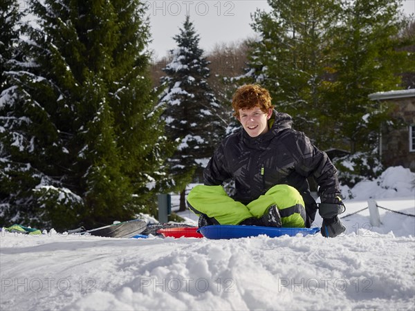 Caucasian teenage boy sledding on snowy hill