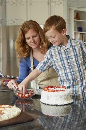 Caucasian mother and son decorating cake in kitchen