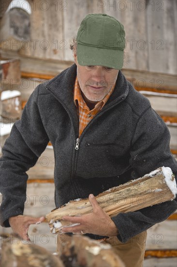 Mixed race man carrying firewood near snowy shed